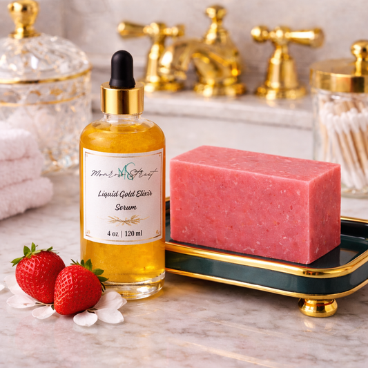 Glass dropper bottle labeled “Liquid Gold Elixir Serum” next to a pink handcrafted soap bar on a decorative tray, with fresh strawberries on a marble countertop and gold bathroom fixtures in the background.