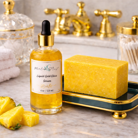 Liquid Gold Elixir Serum paired with a yellow pineapple soap bar and fresh pineapple pieces on a marble countertop with gold bathroom accents